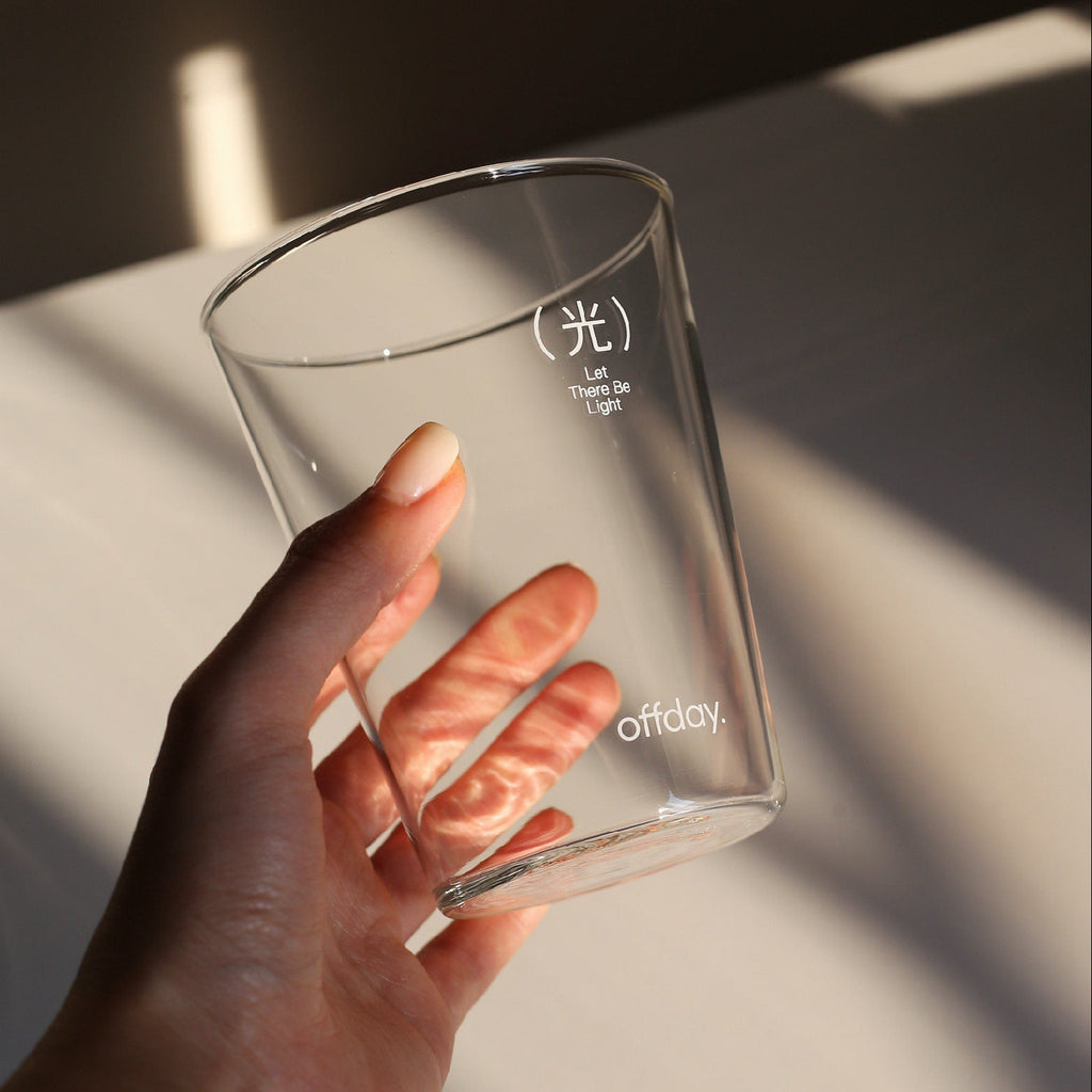 Clear glass cup held by a hand on a light surface with soft shadows